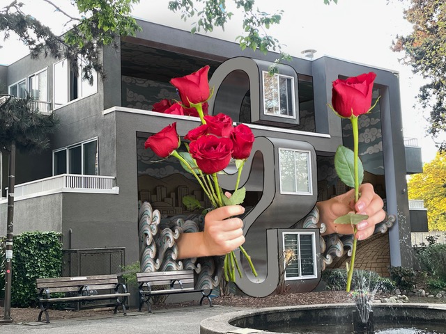 The Gift, a mural on the Laurel Park apartment building: two hands holding red roses over a large number 2 and wave patterns, with benches and a fountain in front.